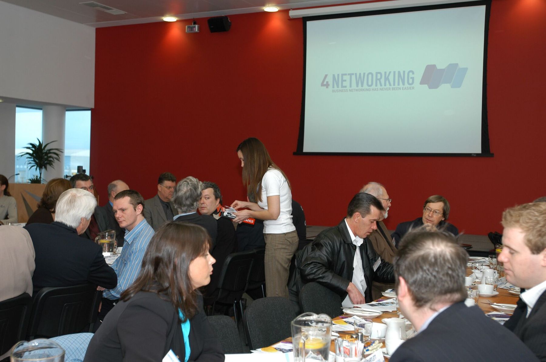 One of the earliest 4Networking breakfast meets - a small group around a table, the original 4Networking 'business networking has never been easier' projection on a red wall