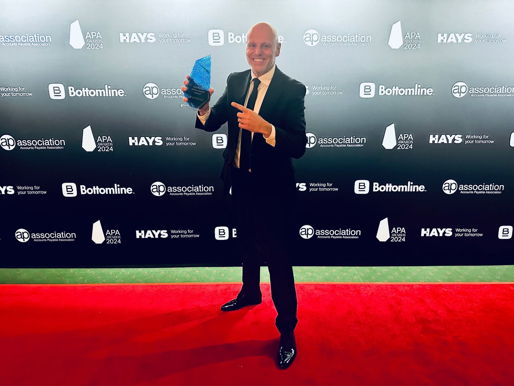 Brad Burton on the red carpet at the APA Awards 2024, holding the Outstanding Achievement Award trophy in front of the sponsor wall