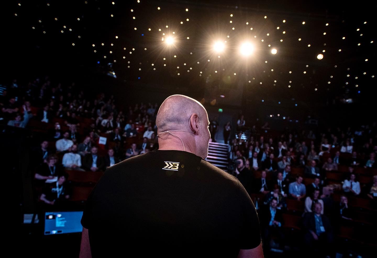 View from behind Brad on stage looking out at a packed auditorium under a starlit ceiling