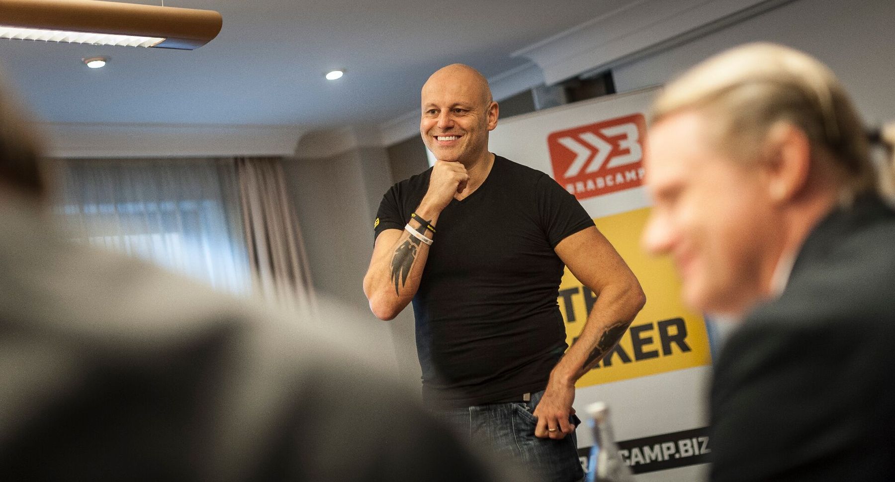 Brad Burton mid-session at Bradcamp, hand on chin, standing in the middle of a tight workshop room with delegates blurred in the foreground