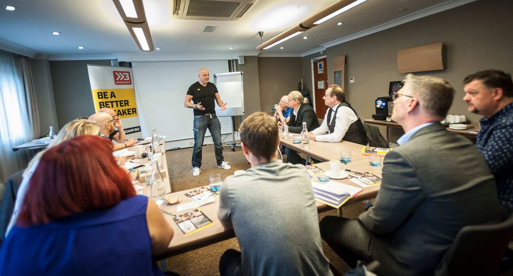 Brad leading a Bradcamp workshop in a hotel meeting room - delegates round tables with notebooks open