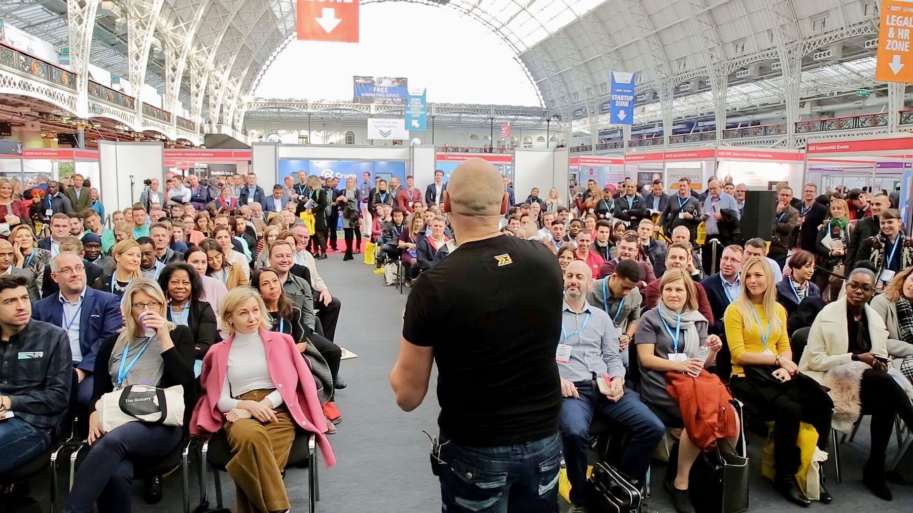 Brad Burton mid-keynote in the round at The Business Show, Olympia London - packed crowd seated all around him