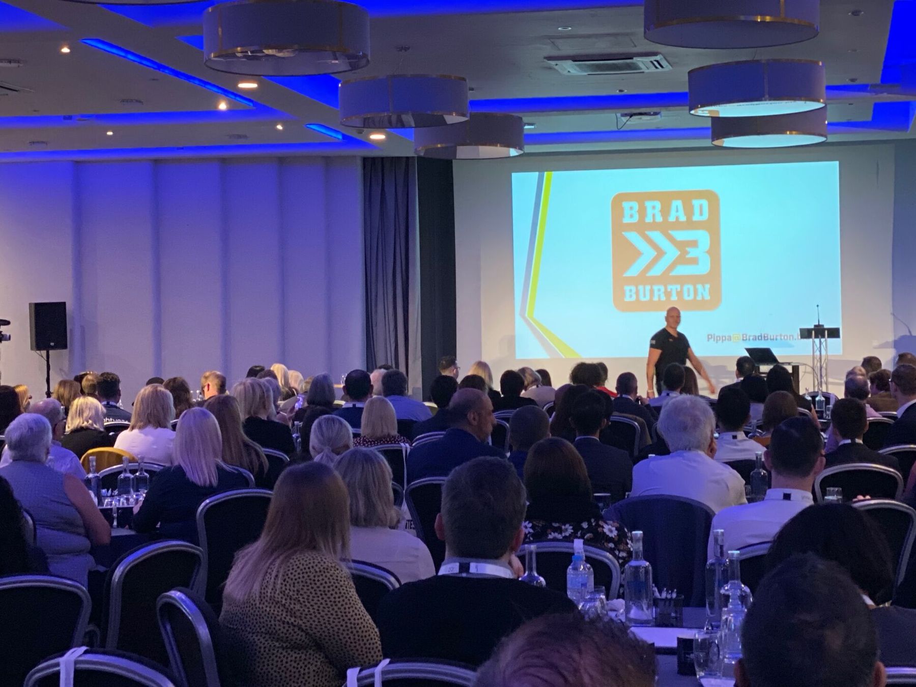 Brad keynoting a packed conference room with the Brad Burton brand on screen