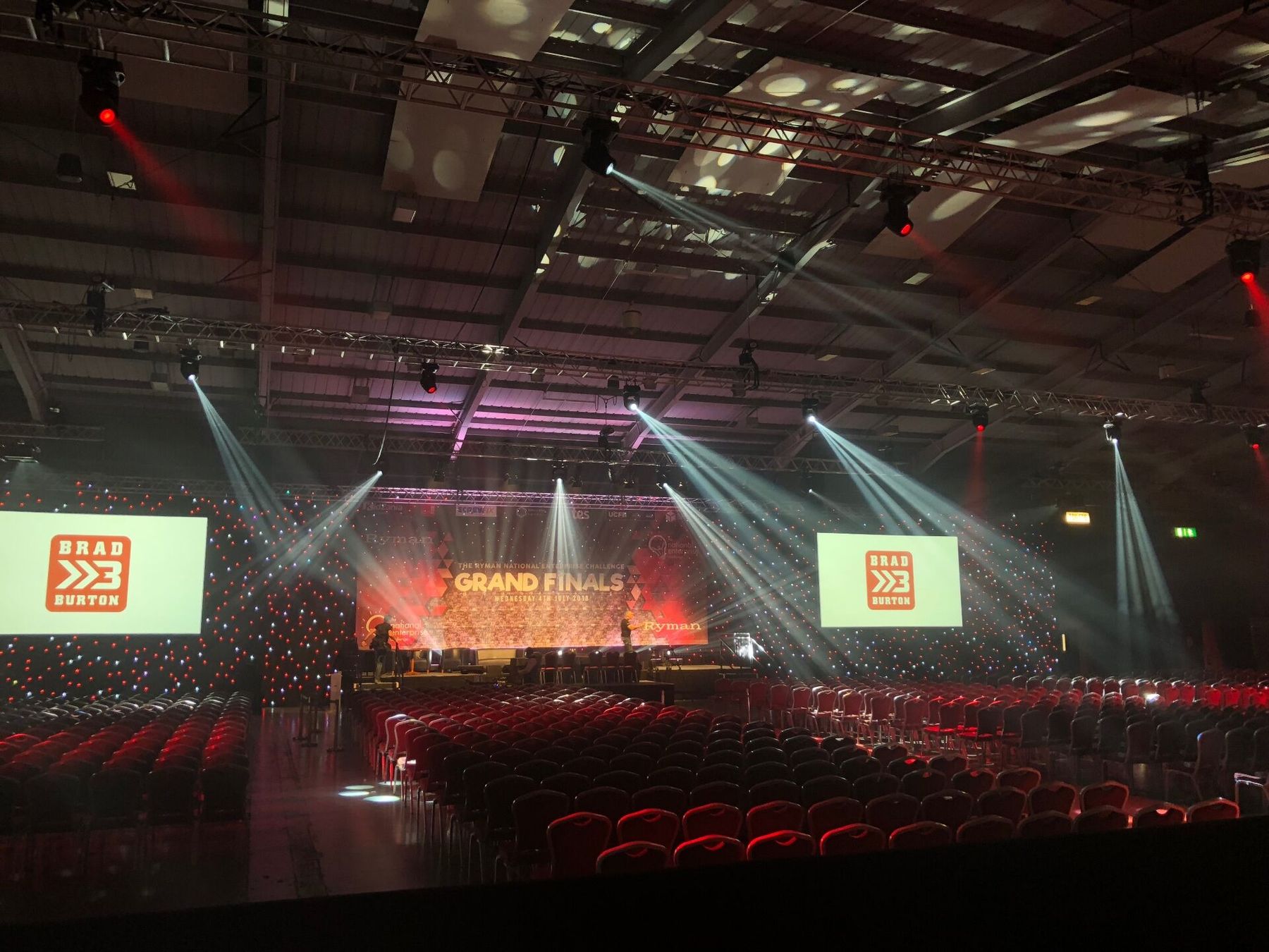 The fully lit Ryman National Enterprise Challenge Grand Finals stage with Brad Burton's logo on the screens, ready for keynote