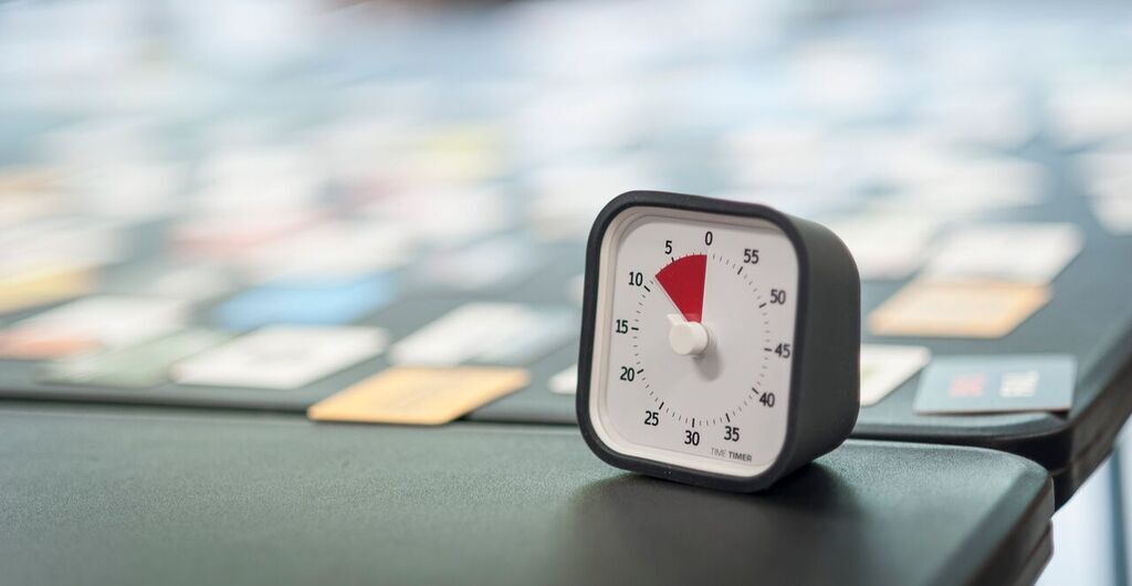 Close-up of Brad's Time Timer ticking down on the edge of a workshop table with blurred cards spread out behind it